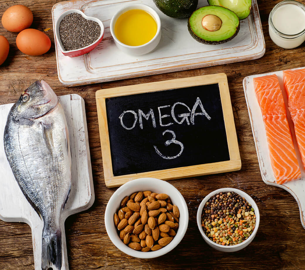 Natural Pharmaceuticals OmegaMarine™ Premium Omega-3 rikkad toiduained nagu kala, lõhe, mandlid, avokaado, chia seemned, munad ja õli puidust lauapinnal.